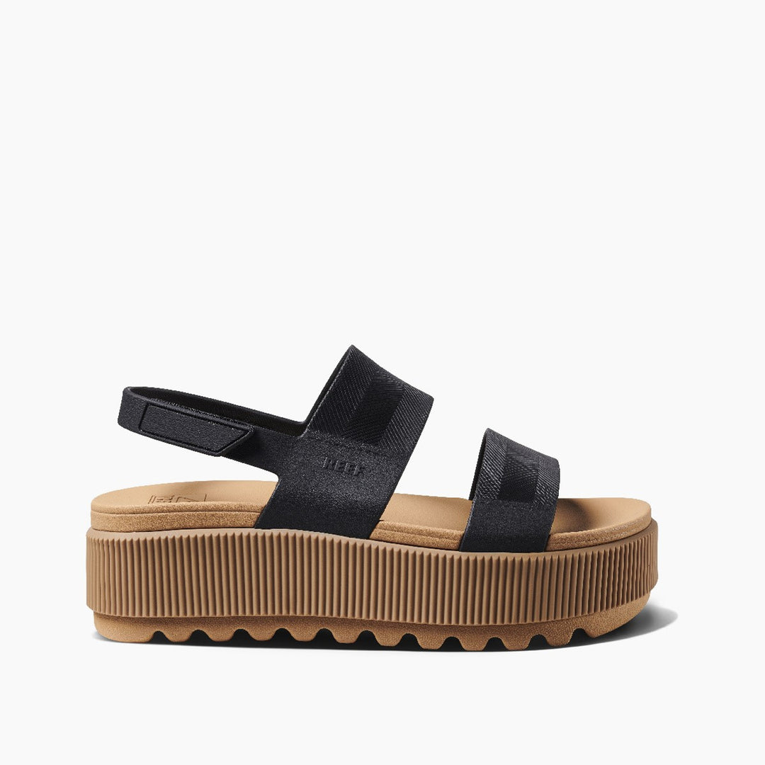 A black and tan platform Reef sandal with adjustable Velcro straps and a thick, lug-designed outsole.