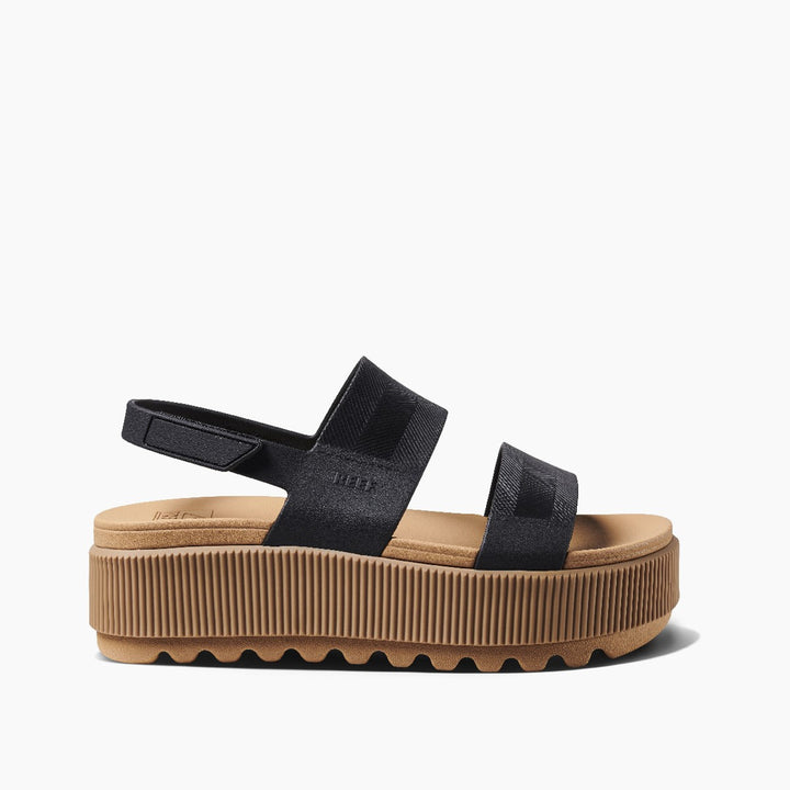 A black and tan platform Reef sandal with adjustable Velcro straps and a thick, lug-designed outsole.