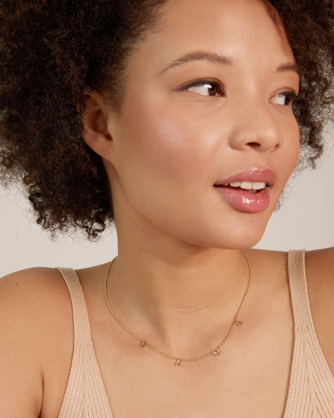 Woman wearing delicate gold chain necklace with letter charms spelling MAMA