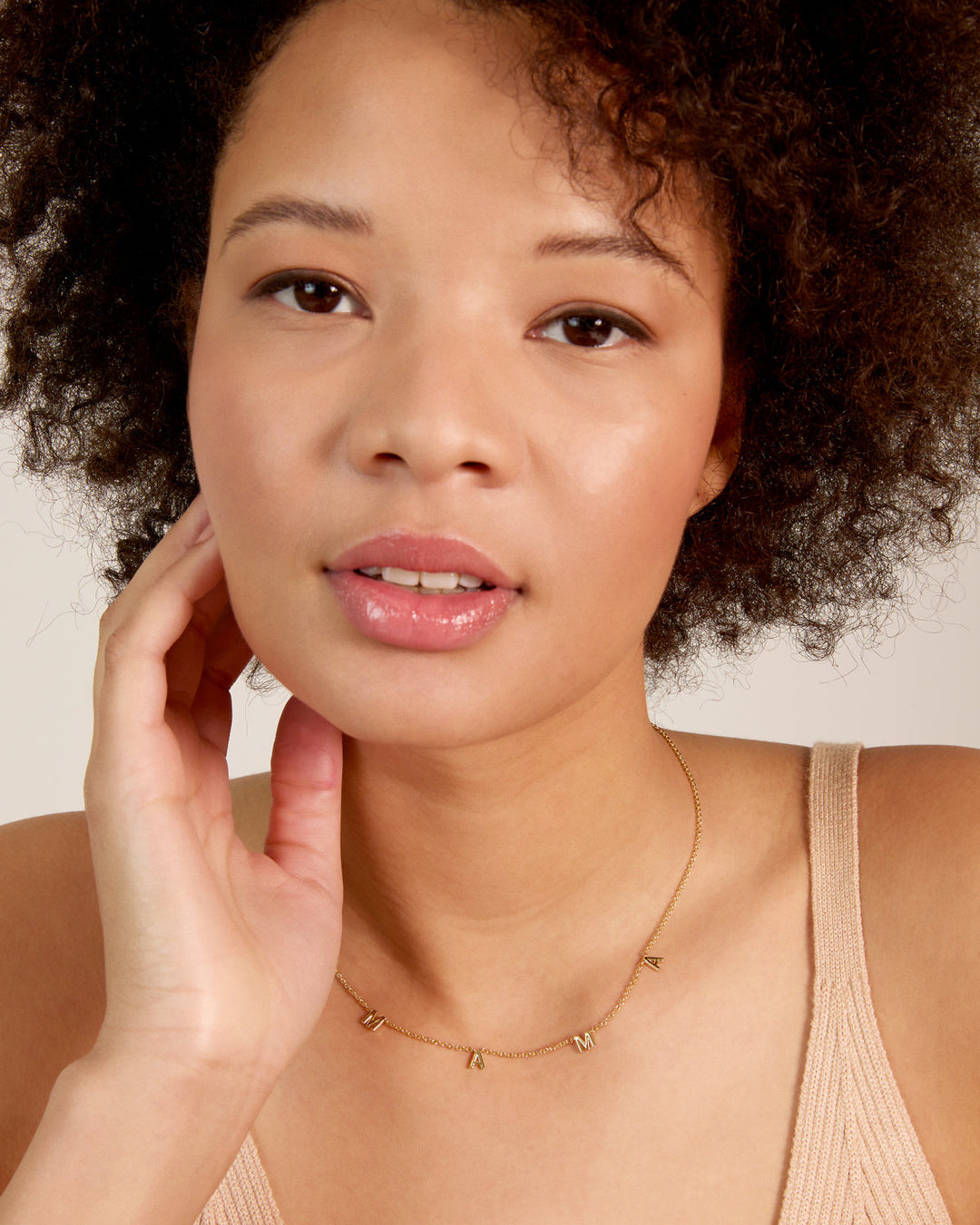 Woman wearing delicate gold chain necklace with letter charms against neutral background