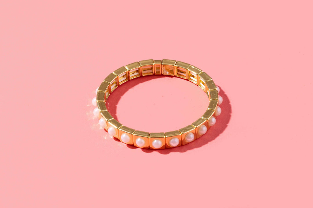 Gold stretch bracelet with white pearl beads on pink background