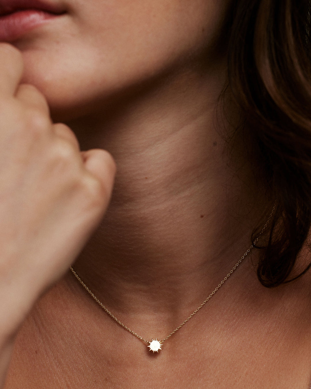 Gold sun pendant necklace worn on model's neck against warm lighting