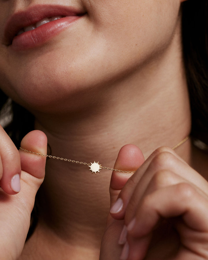 Model wearing delicate gold chain necklace with small sun pendant charm
