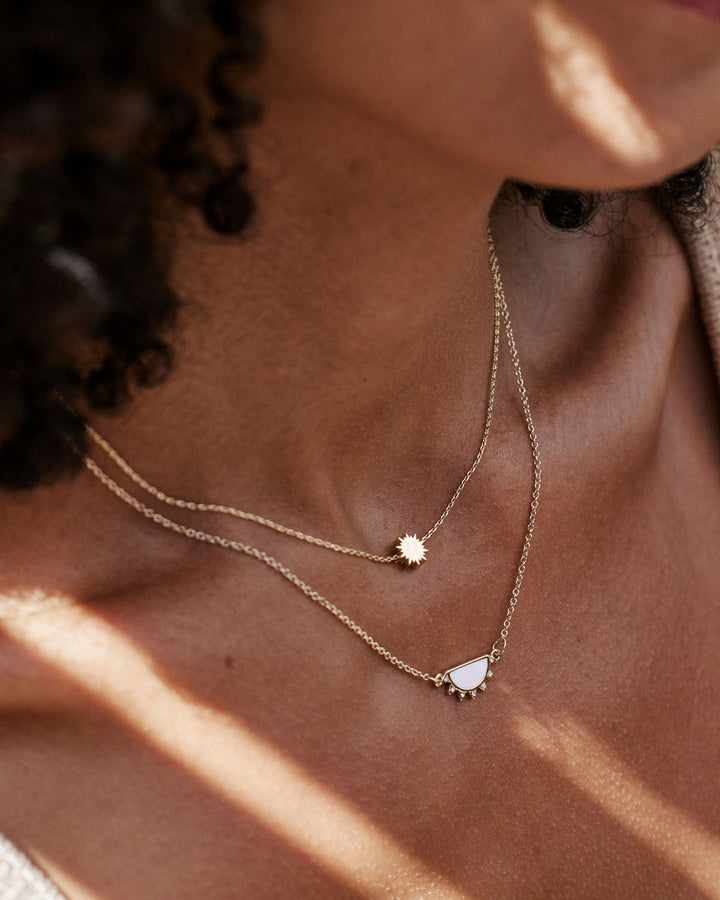 Layered gold necklaces with sun charm and white stone pendant on model