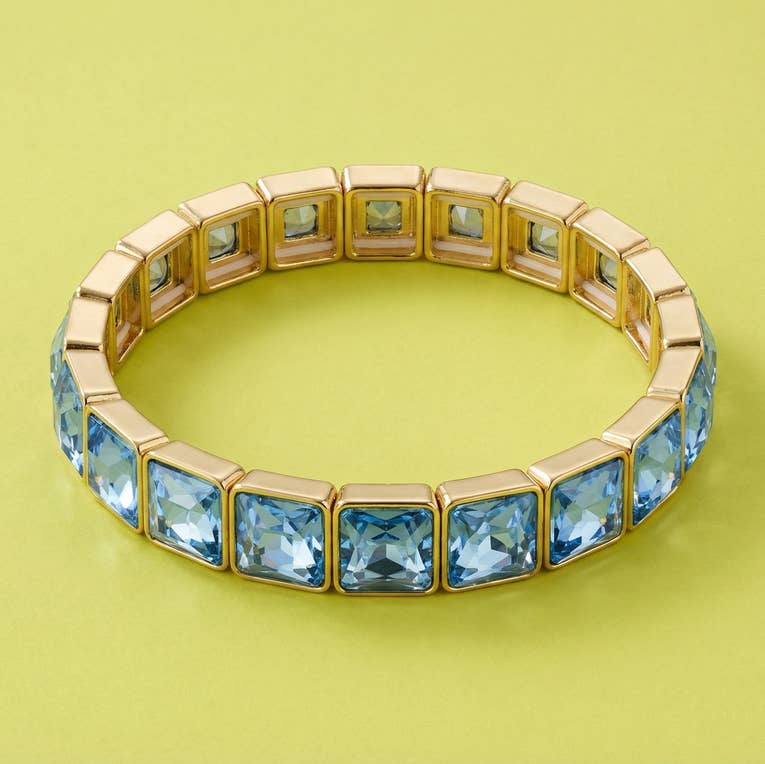 Gold stretch bracelet with square light blue gemstone segments on yellow background