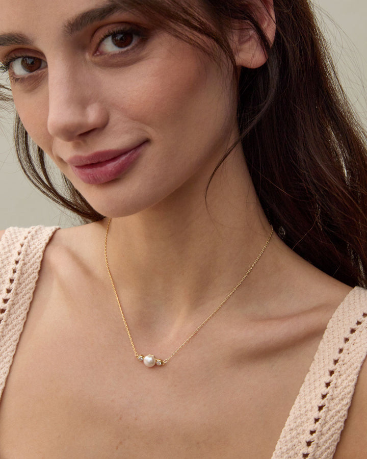 Woman wearing delicate gold chain necklace with single white pearl pendant
