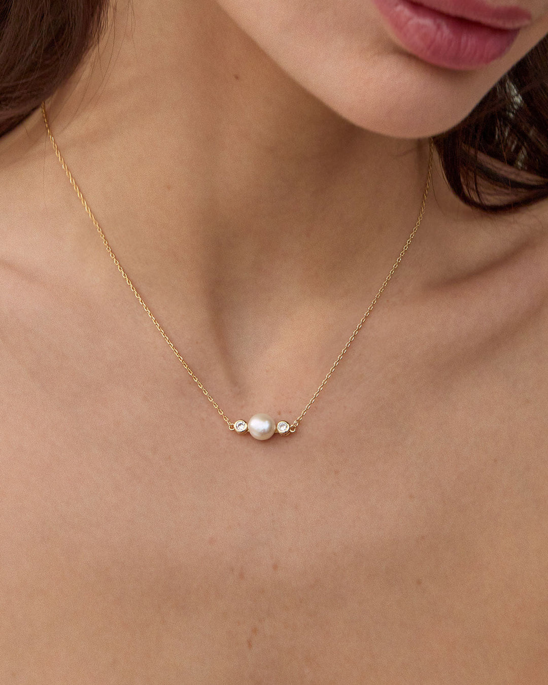 Gold necklace with white pearl and diamond accents worn by model