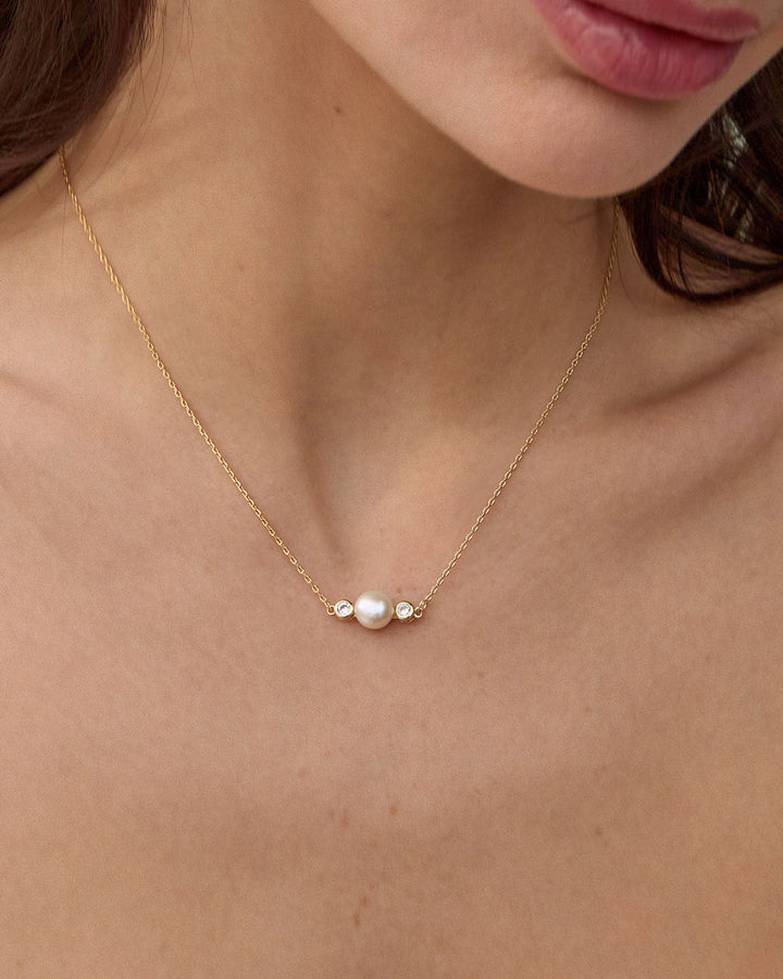 Gold necklace with white pearl and diamond accents worn by model