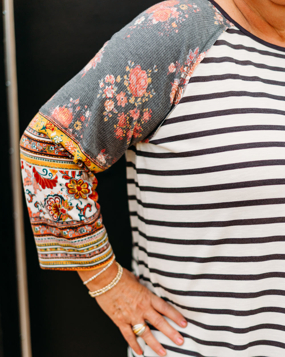 Person wearing a striped shirt with a floral elbow patch on a black background