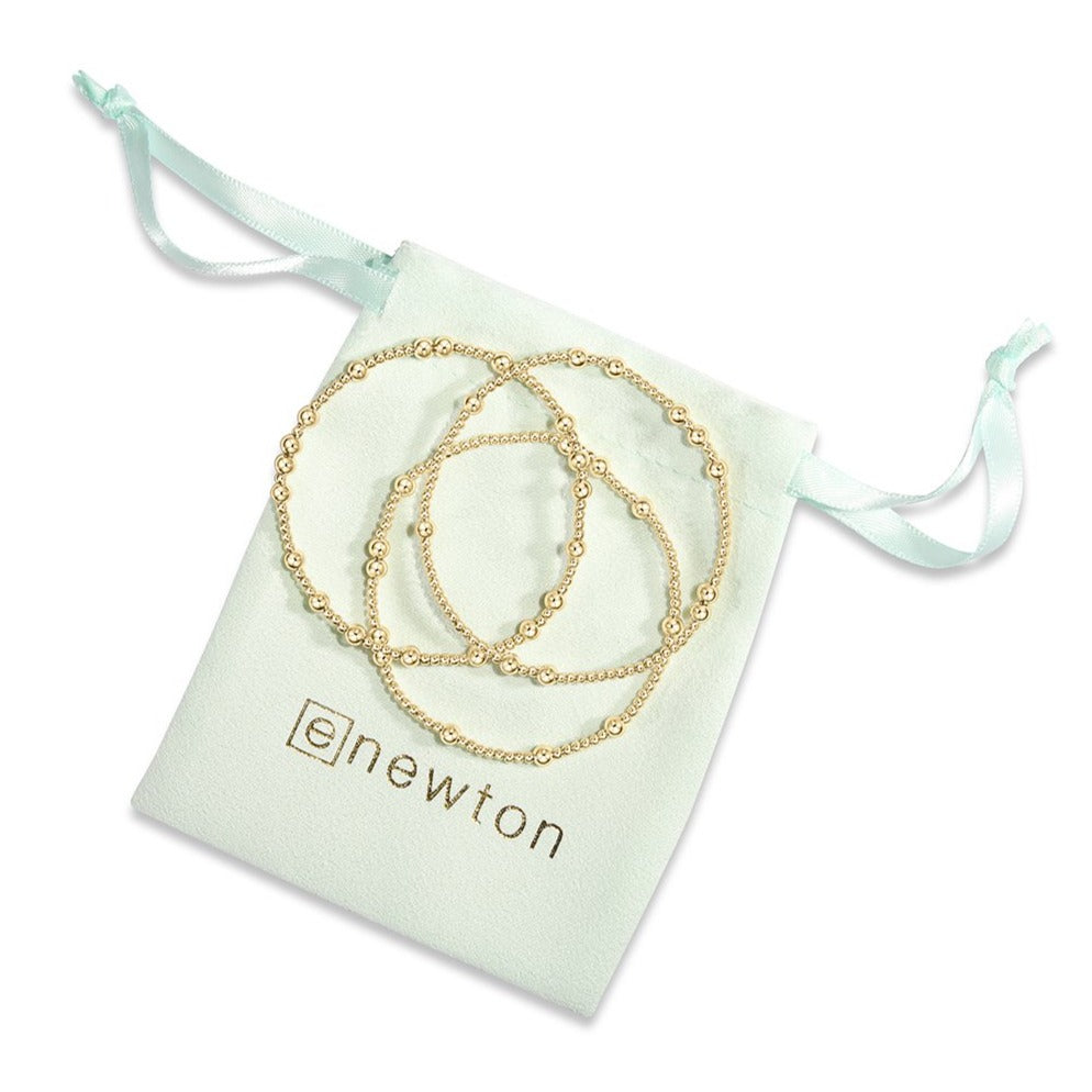 Enewton gold beaded bracelets in three sizes displayed on mint green drawstring pouch