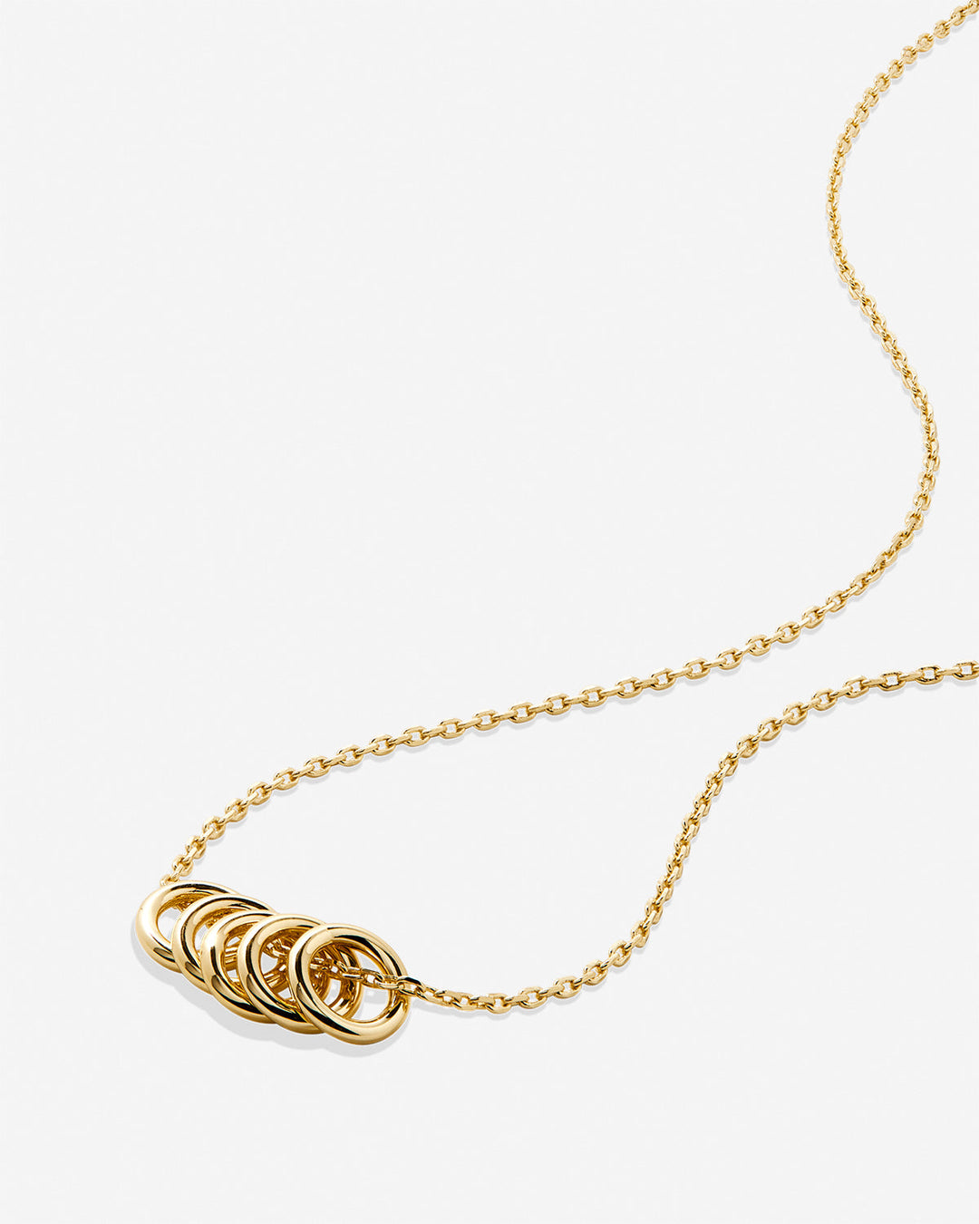 Gold chain necklace with interlocking circular rings pendant on light background