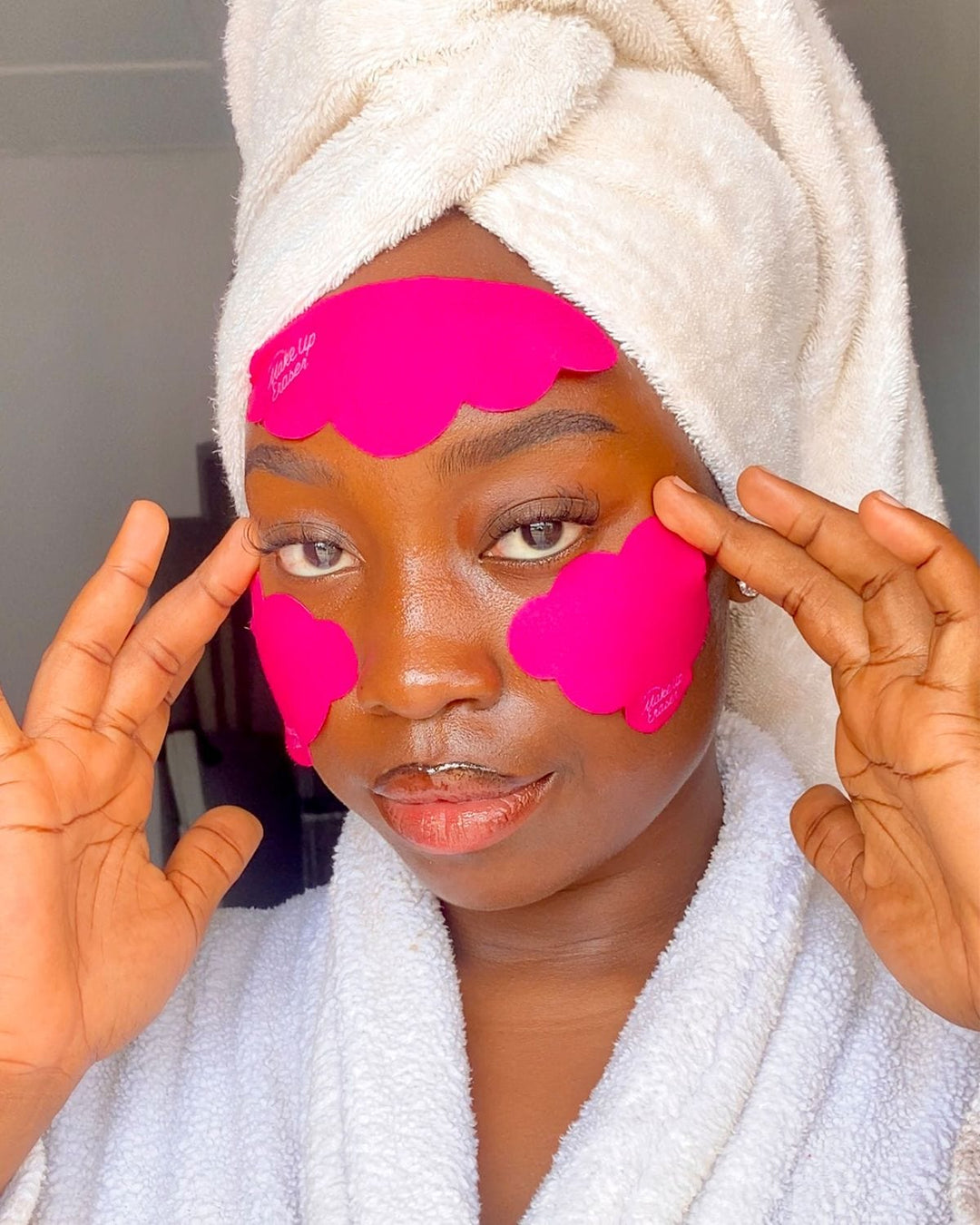 Woman wearing bright pink reusable under eye patches in white bathrobe