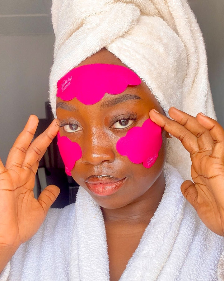 Woman wearing bright pink reusable under eye patches in white bathrobe